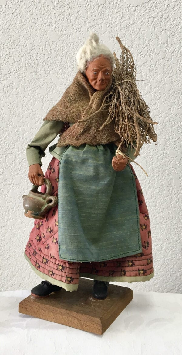 A small statue of an old woman holding a tea pot and sticks