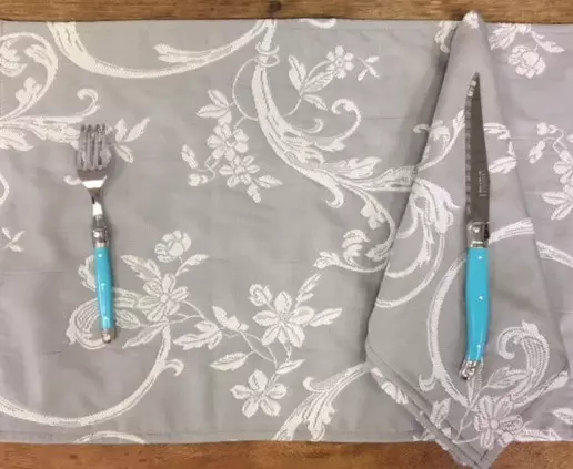 A grey placemat with white vine designs and blue utensils