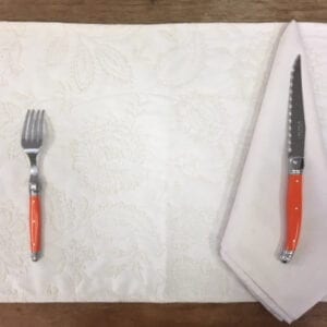 A white placemat with orange utensils